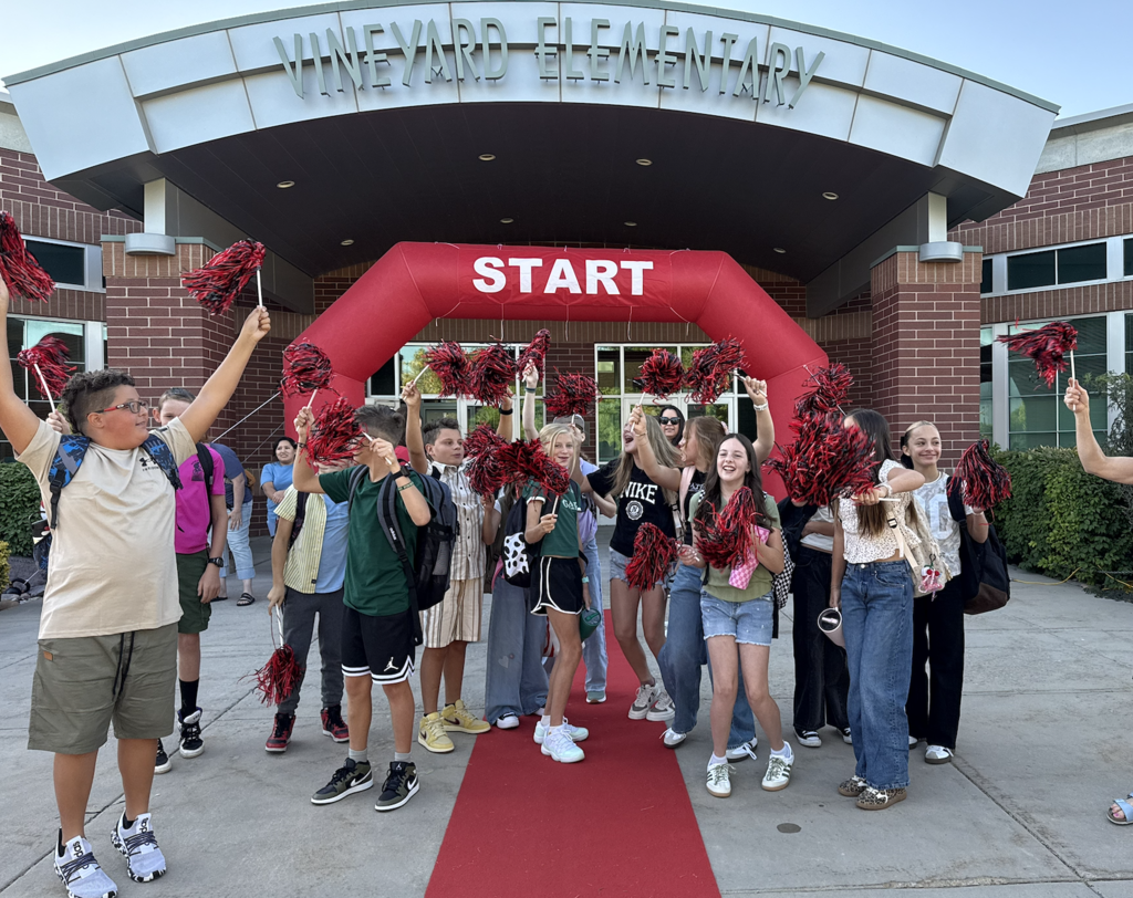 6th grade students in front of the school shaking black and red pom poms