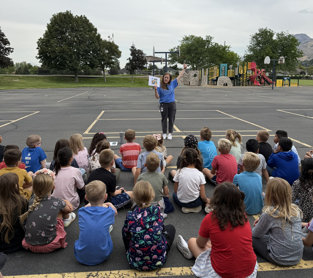 Image of Mrs. Knight teaching students sitting on the blacktop about the rules of Orchard's playground.