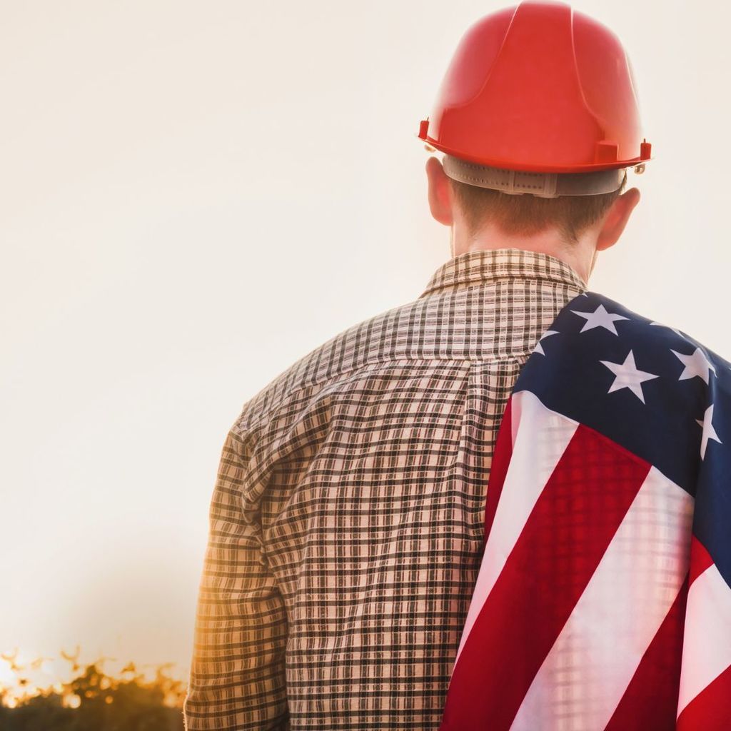 Worker wearing a hard hat with an American Flag draped over his shoulder.