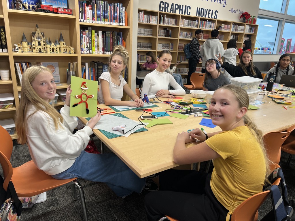 Students in the library showing craft projects they made.