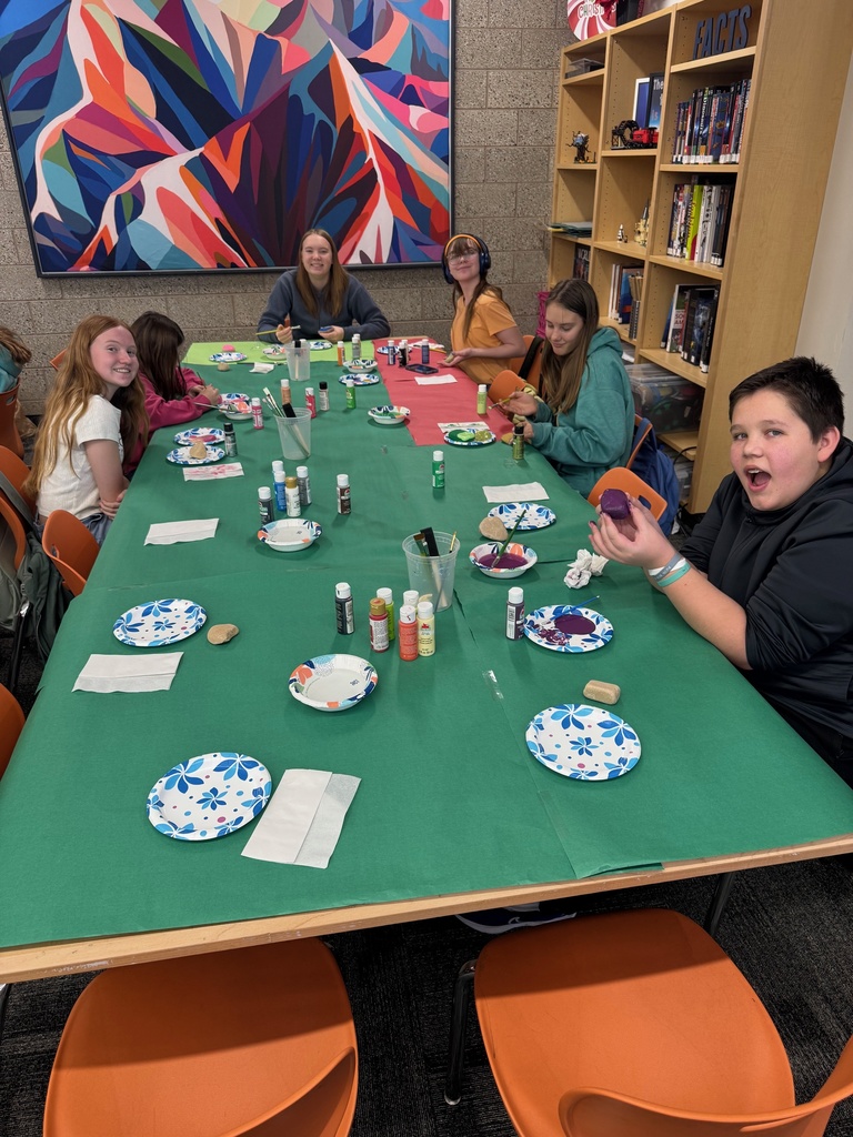 Smiling students painting rocks at a table covered in green paper.
