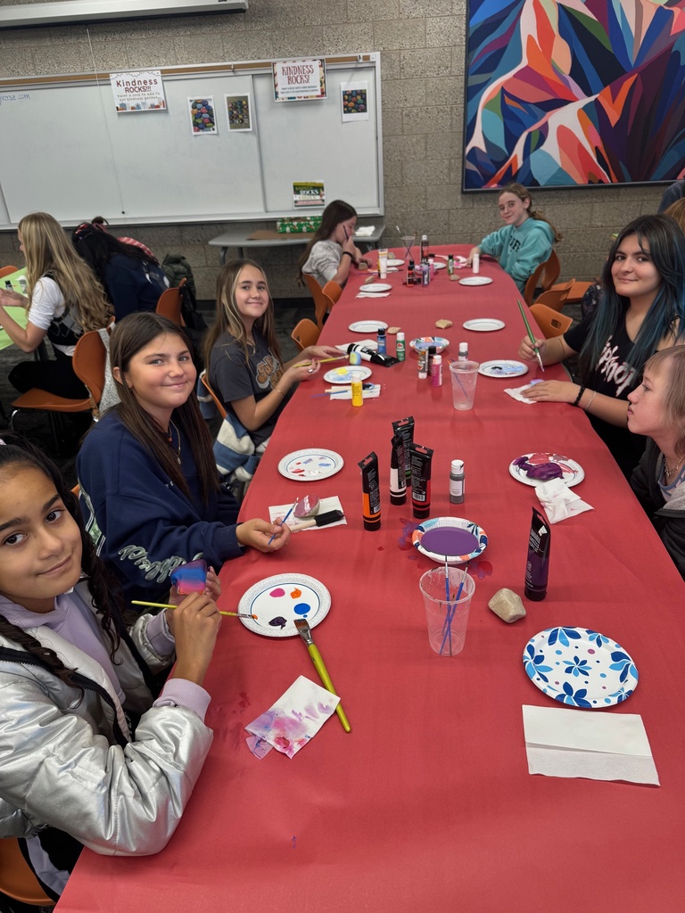 Smiling students painting rocks at a table covered in red paper.