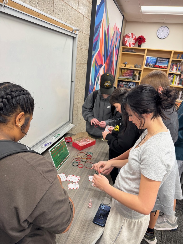 5 students looking down as they tie cards to candy canes with ribbons.