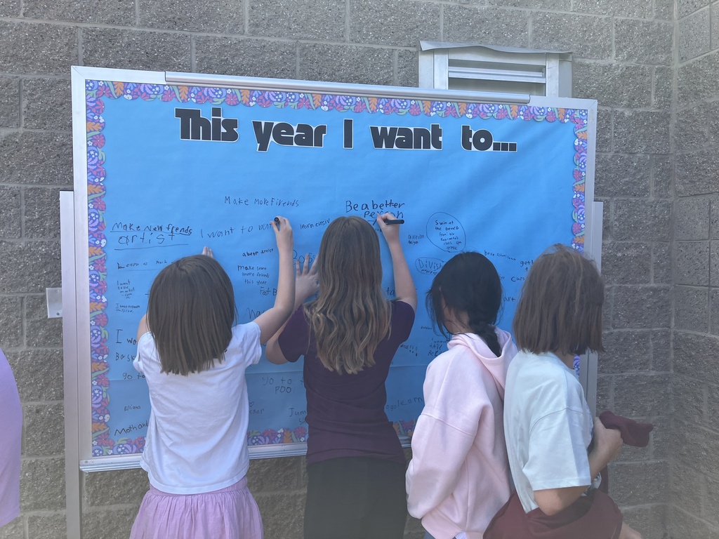 4 students standing at a bulletin board with blue paper writing. The title on the board is "This year I want to"