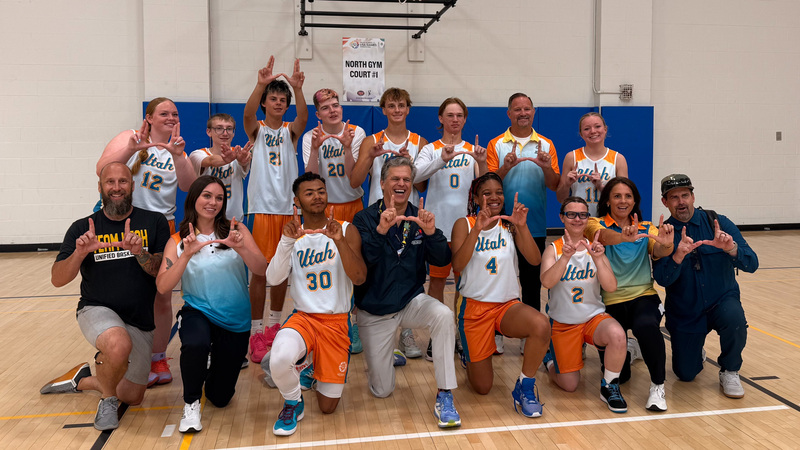Alpine students representing Team Utah posing for a photo with the hands held up in U shapes, on a basketball court, wearing their Utah basketball jerseys at the Special Olympics USA games