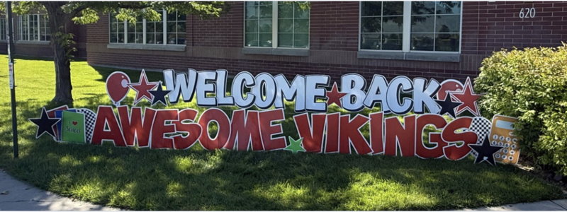 outside the brick school and a yard sign that is black and red and says welcome back awesome vikings