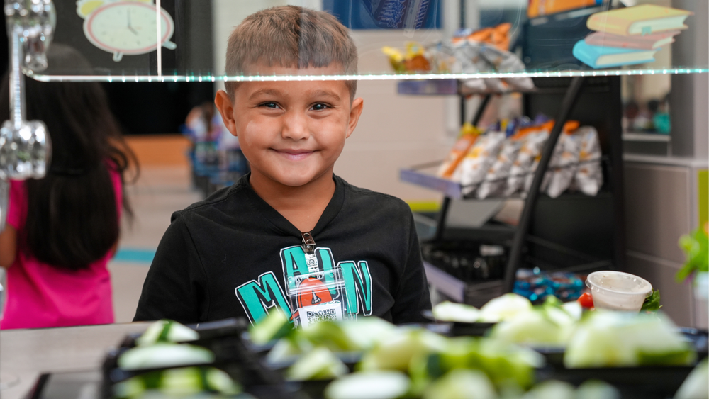 Alvin Elementary student smiling at lunch in front of salad