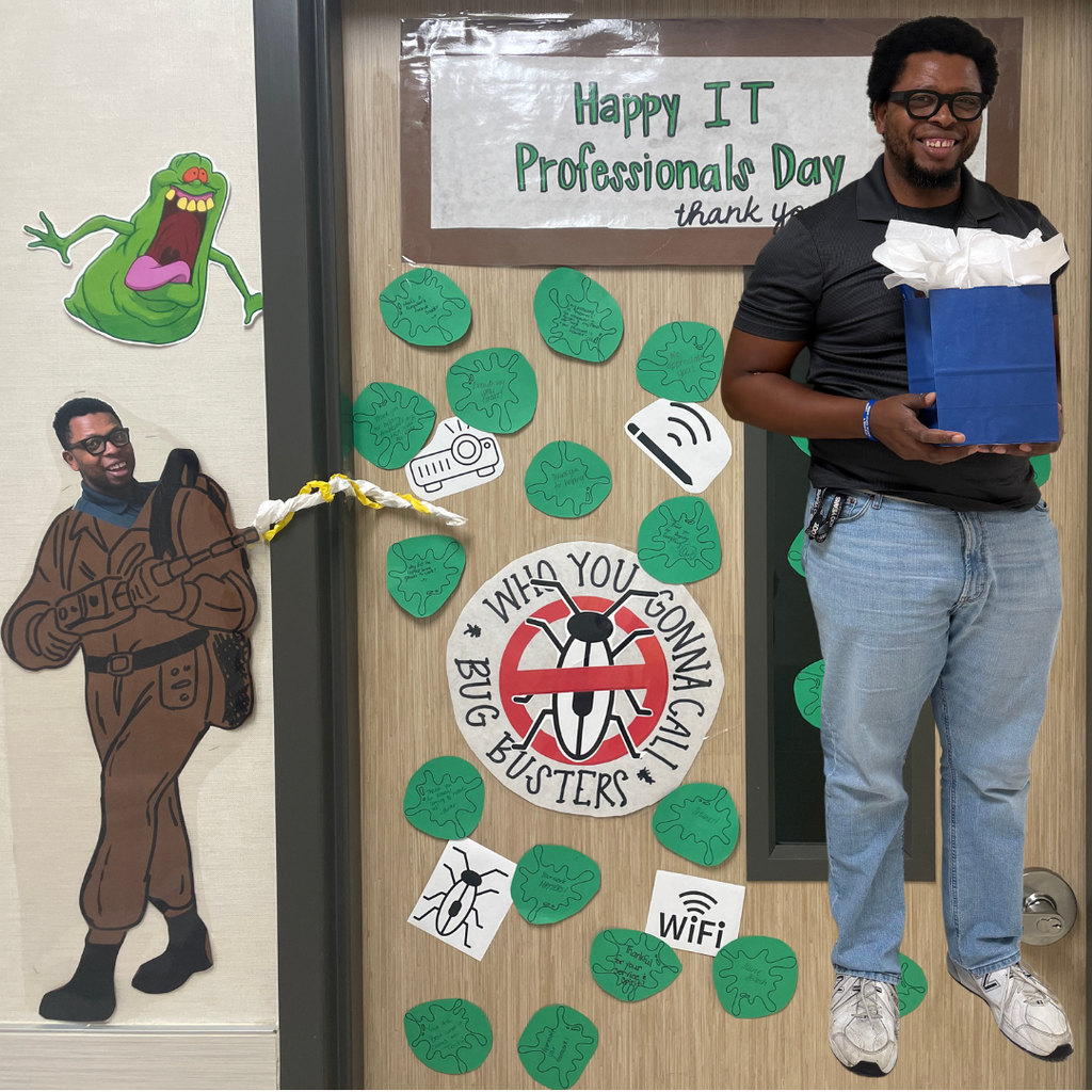 Door has two signs reading, "Happy IT Professionals Day" and "Who You Gonna Call? Bug Busters"  Ghost buster figure and slimer going after the IT bugs.  Our IT Professional, Mr. Ghazi standing in front of the door holding a gift bag.
