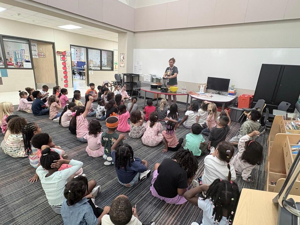 Ms. Hunter standing in front of all the kindergarten students on the carpet.  She is leading them through procedural text on how to make applesauce.