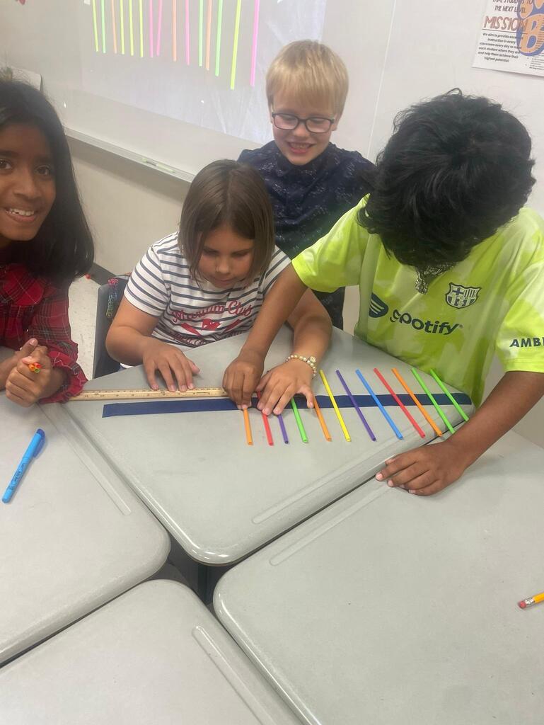 Students working together collaboratively at desks.   they are using tape, rulers, and straws to create sound waves.