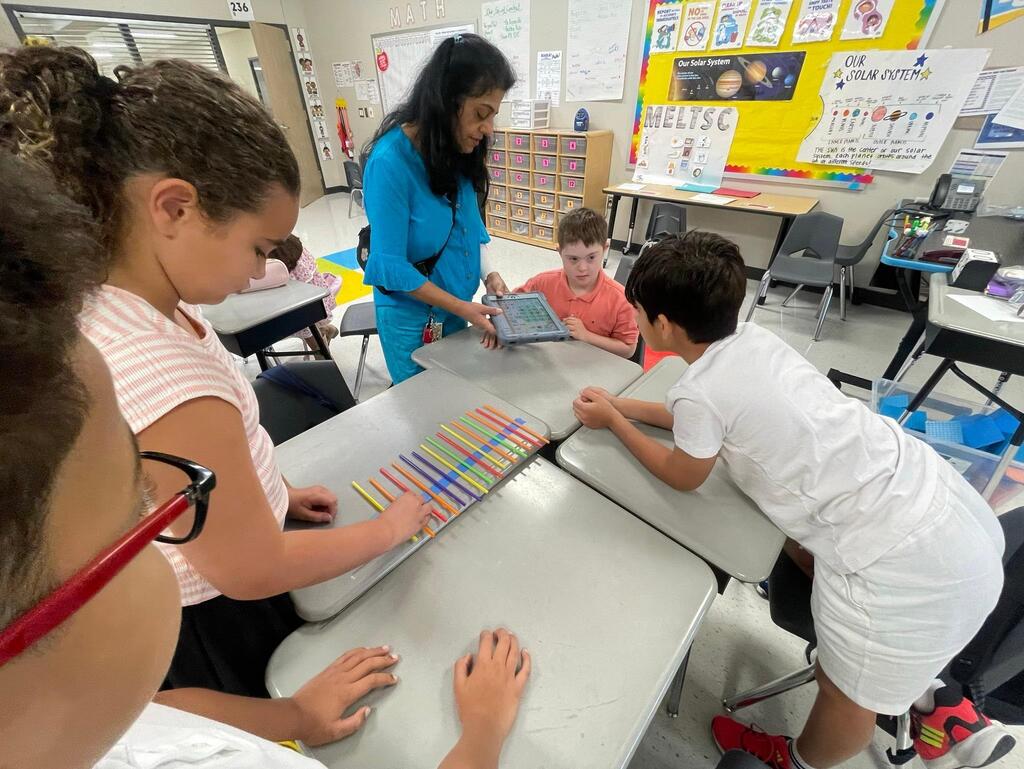 Students working together collaboratively at desks.   they are using tape, rulers, and straws to create sound waves.