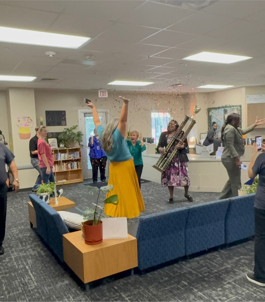 admin team celebrating in the office with confetti as they receive the traveling district trophy for best attendance
