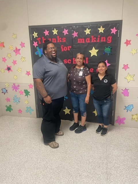 Three of our custodial staff posing together in front of their decorated door.