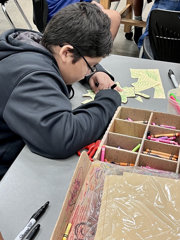 A middle school student wearing glasses and a dark hoodie working on a fall texture plate printing art project at a table.