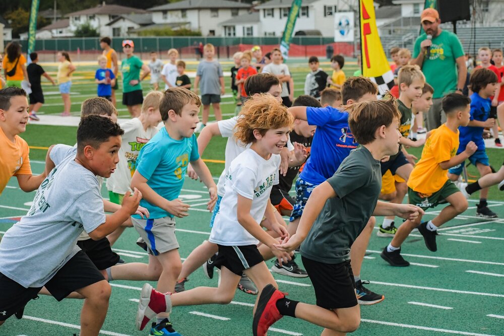 Young Comets running on the green track at the high school with smiling happy faces