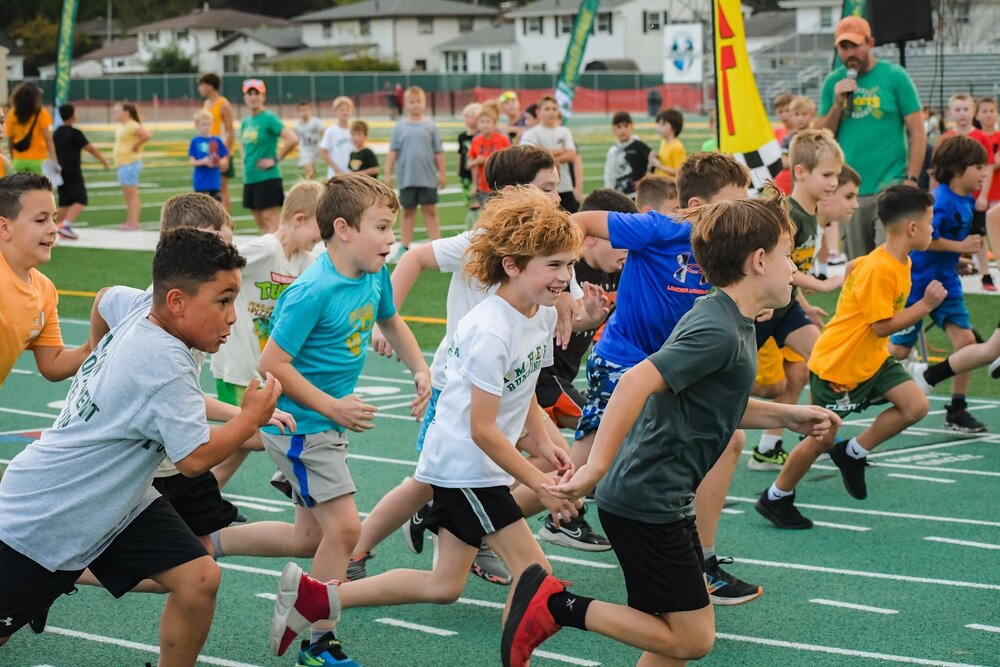 Young Comets running on the green track at the high school with smiling happy faces