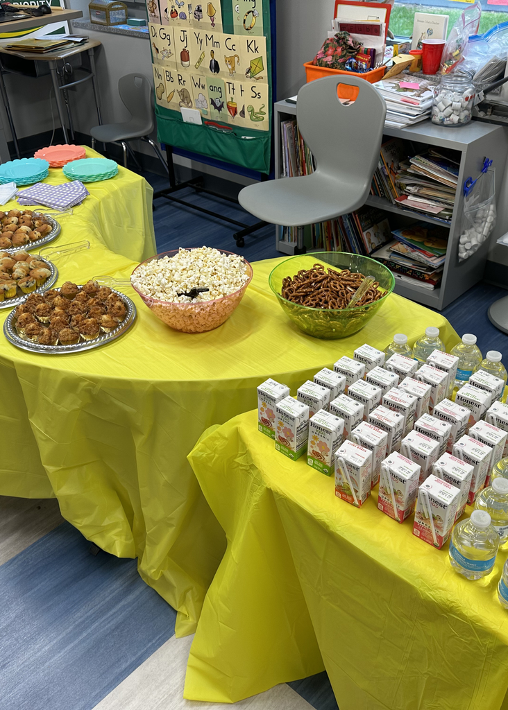 Table of snacks to fulfill the Cafe part of the event. Pop corn, pretzels, juice, water, and more on a yellow table cloth