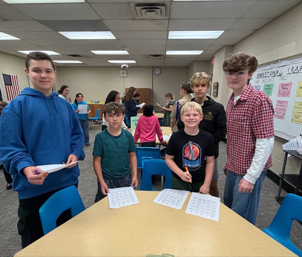 Four students from Nord Elementary and Marion L. Steele High School gather around a table during Marion Mentoring. The students smile for a photo with bingo activity sheets in front of them.