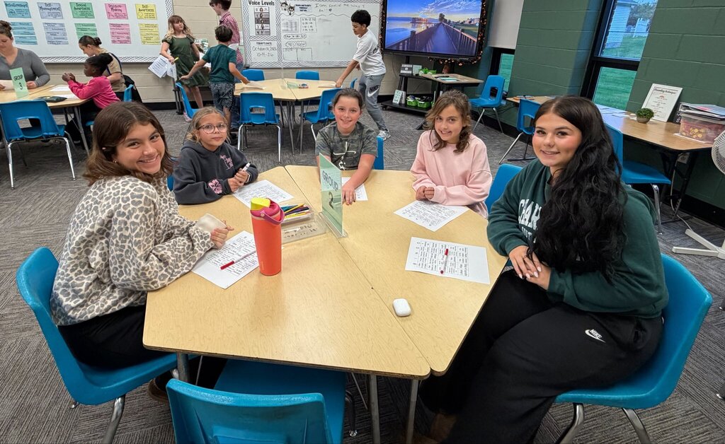 Five students smile around a classroom table while participating in Marion Mentoring at Nord Elementary. Bingo sheets and markers are spread across the table as older and younger Comets enjoy time together.