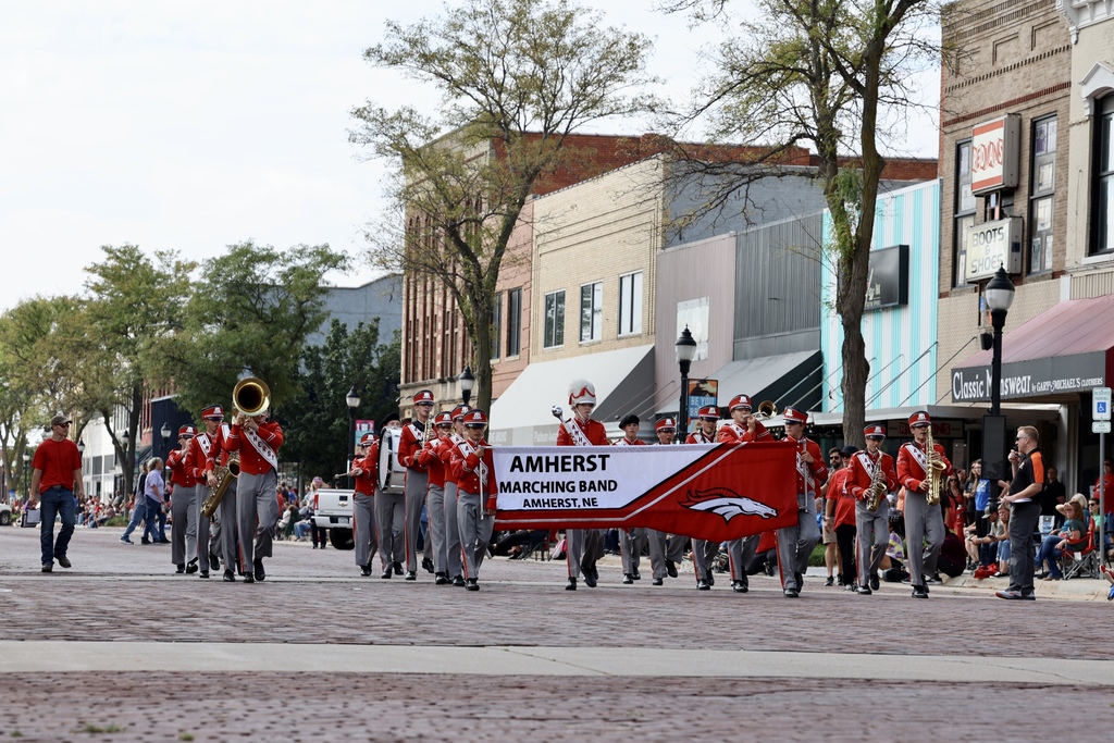 The Amherst band marches down a street. Kids in front hold the Amherst banner