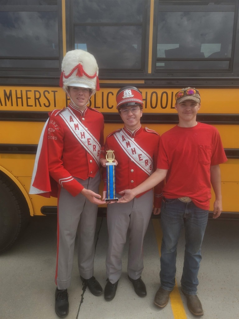 3 senior in red pose in front of a school bus with a blue and gold band trophy