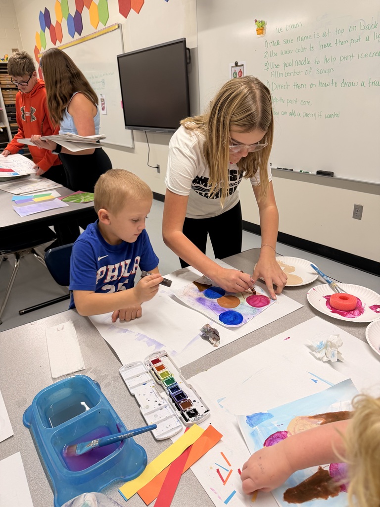 Older students help younger students create food themed artwork