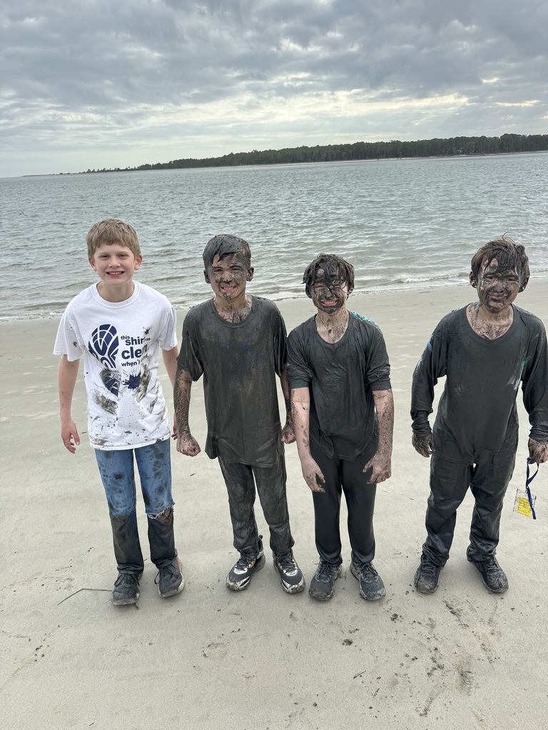 4 boys on the beach showing off their mud from the mudpit!