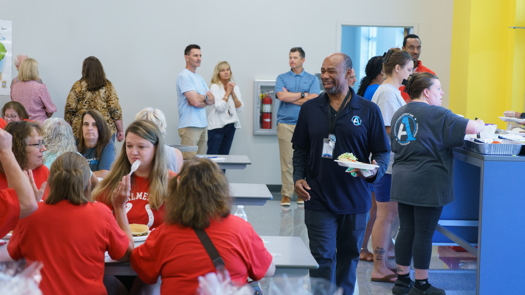 A staff member smiles with a plate of food as he walks past a table of colleagues