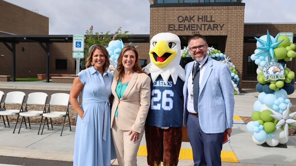Staff members, the eagle mascot, and the state superintendent of education pose for a photo in front of the new school