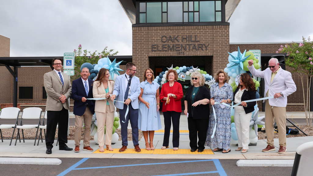Members of the school board, staff members, and the state superintendent of education smile after cutting the ribbon for the new school