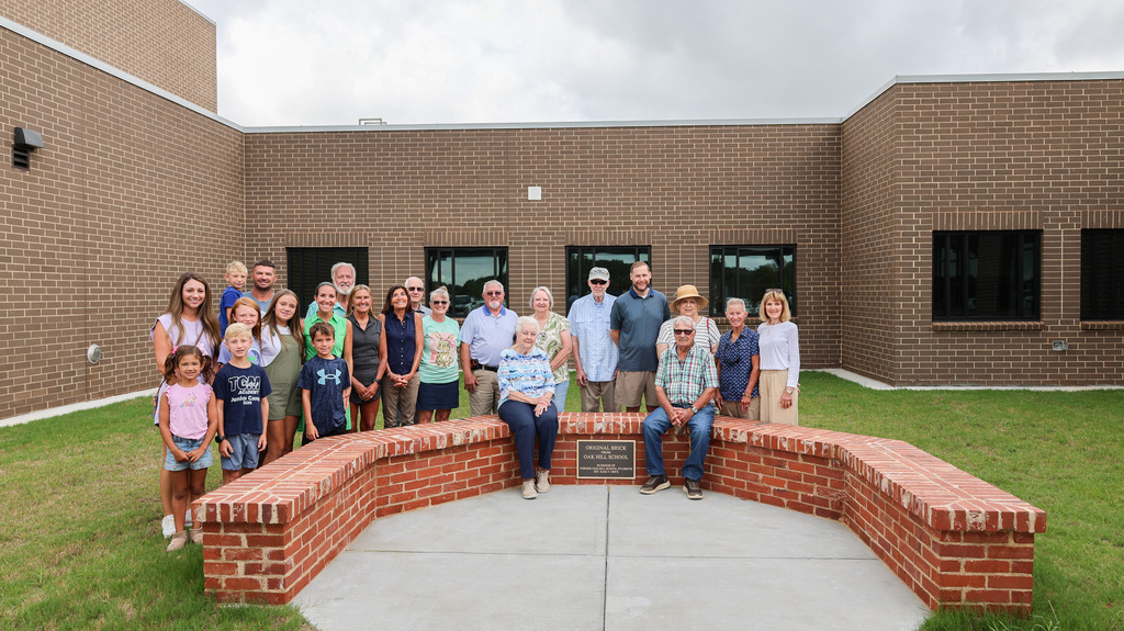 Members of the community pose for a picture on the bench honoring the former Oak Hill school