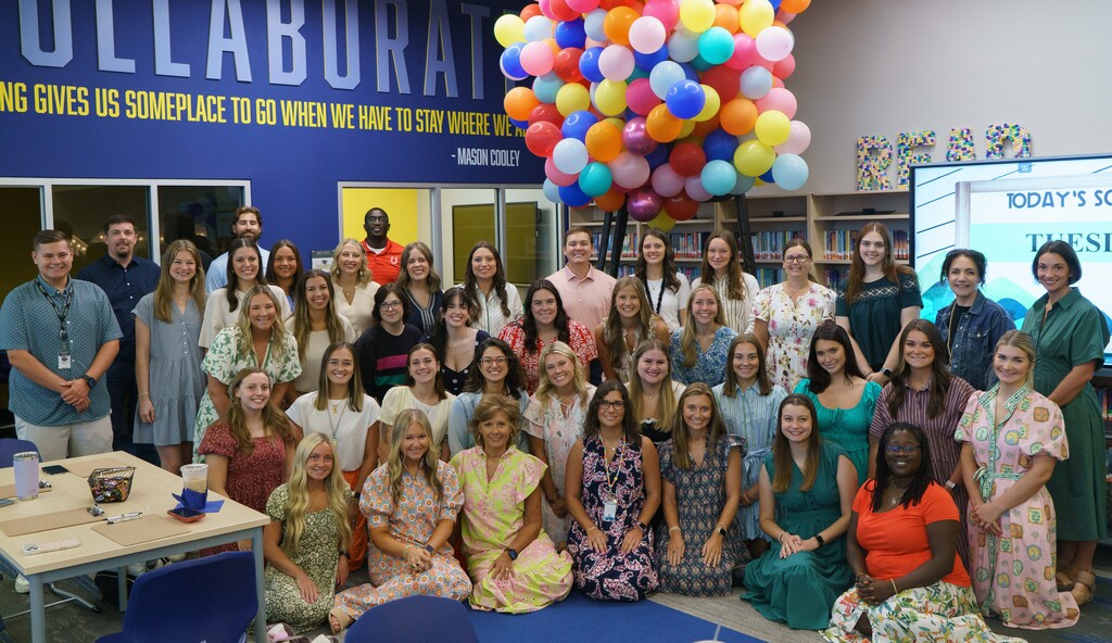 The new induction teachers smiling for a group photo in front of balloons