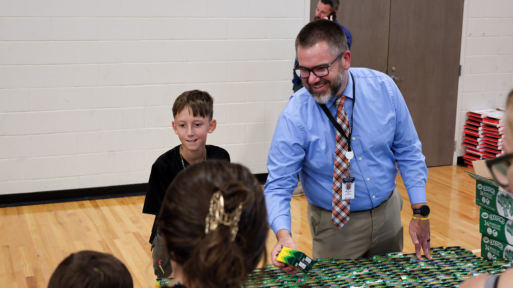 A staff member and student smile as they hand out crayons