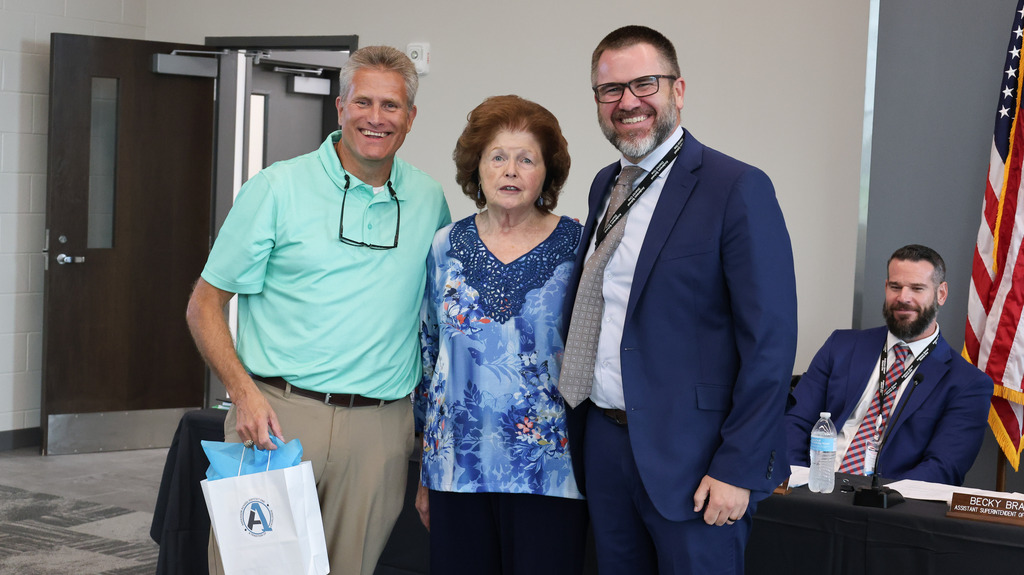 The former superintendent, board chair, and current superintendent smile and pose for a picture