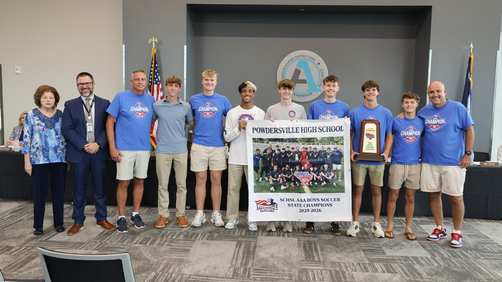 The Powdersville High School boys soccer team poses for a photo with the superintendent and board chair with a banner recognizing them for winning the 3A state championship