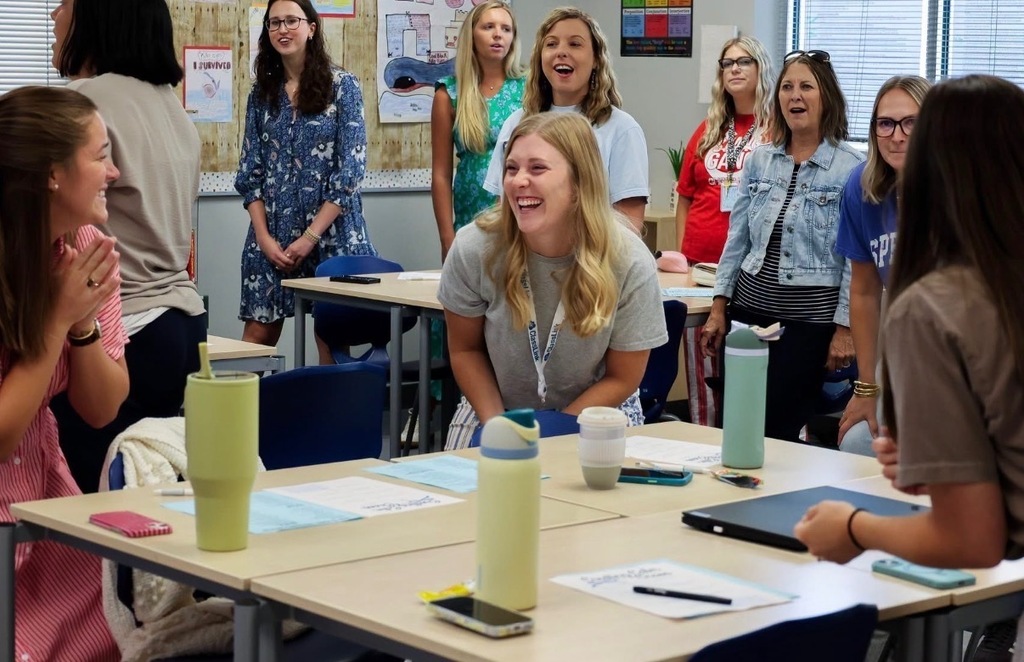 Elementary school teachers participate in a lively professional development activity, smiling and collaborating in a classroom as they prepare for the new school year.