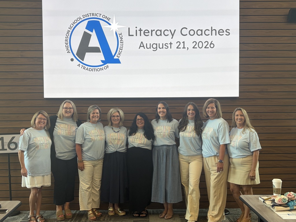 Our literacy coaches pose for a picture and smile in front of a board that says Literacy Coaches August 21, 2026
