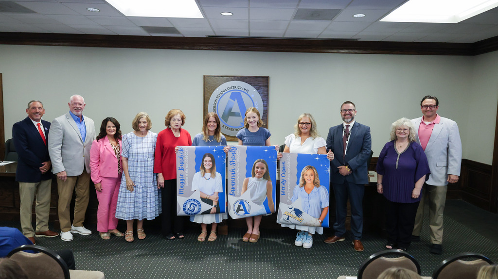 The school board poses for a picture with the district employees of the year holding their recognition banners
