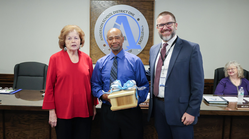 The board chair and superintendent pose with the coordinator of custodial services after recognizing him for his dedication to our schools