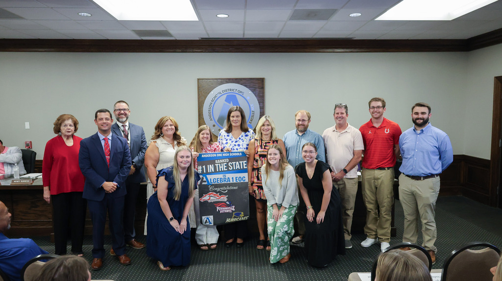 District and school board leaders pose with algebra 1 teachers posing with their recognition banner for their #1 ranking on the EOC