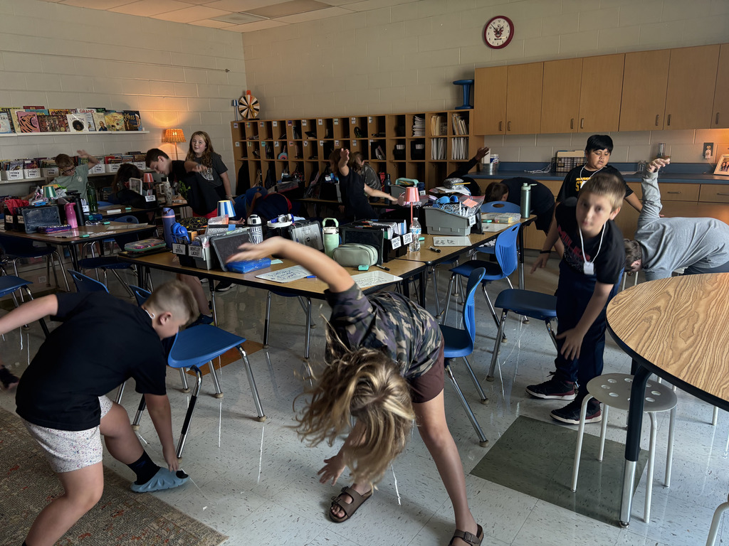 Students participate in a movement activity beside their desks in the classroom.