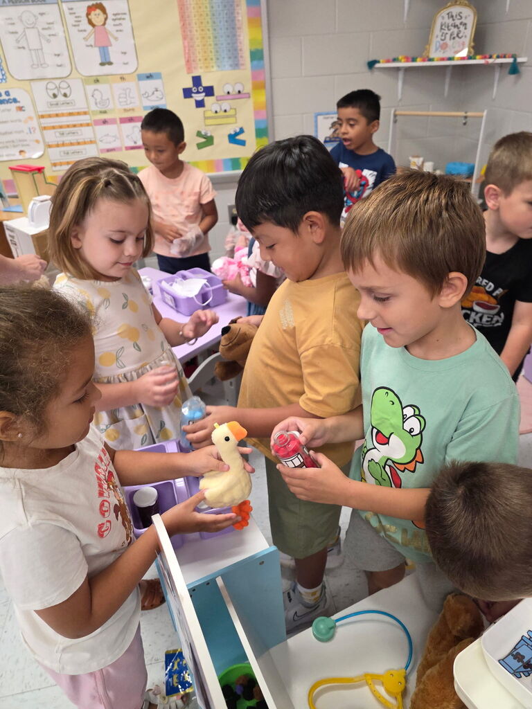 Students engage in pretend play at a classroom veterinary clinic using stuffed animals and medical supplies.