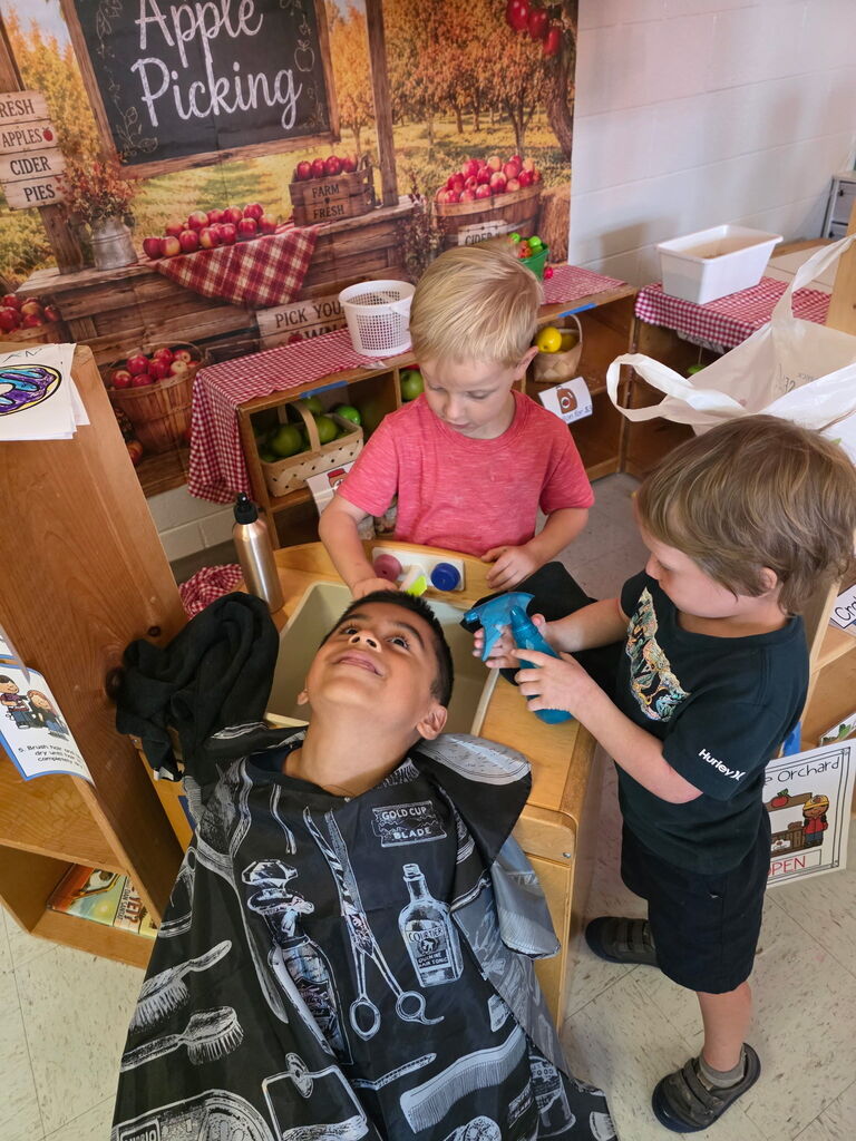 Students pretend to operate a barbershop during classroom dramatic play.