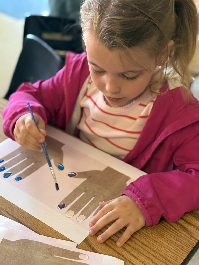 A student focuses on painting nails at a nail salon during community helpers activity.