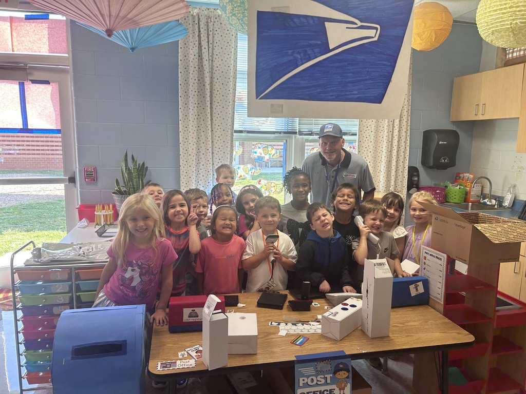 Students pose with a Spearman's own "real mailman"  behind a classroom post office center during a hands-on learning activity.