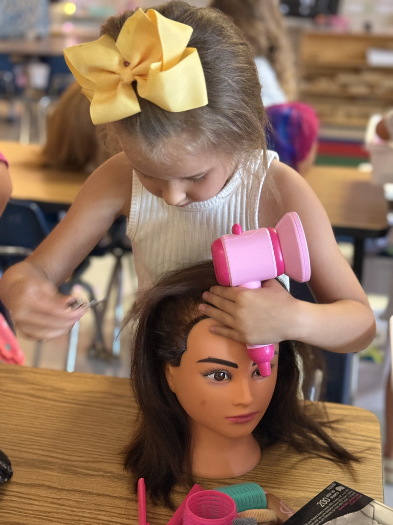 A student practices hairstyling on a mannequin head during a classroom community helpers activity.