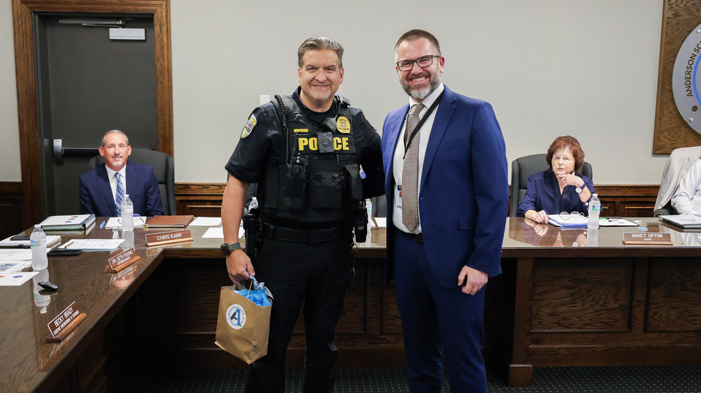 The superintendent and SRO pose for a picture during a board meeting after the SRO was honoring for going above and beyond