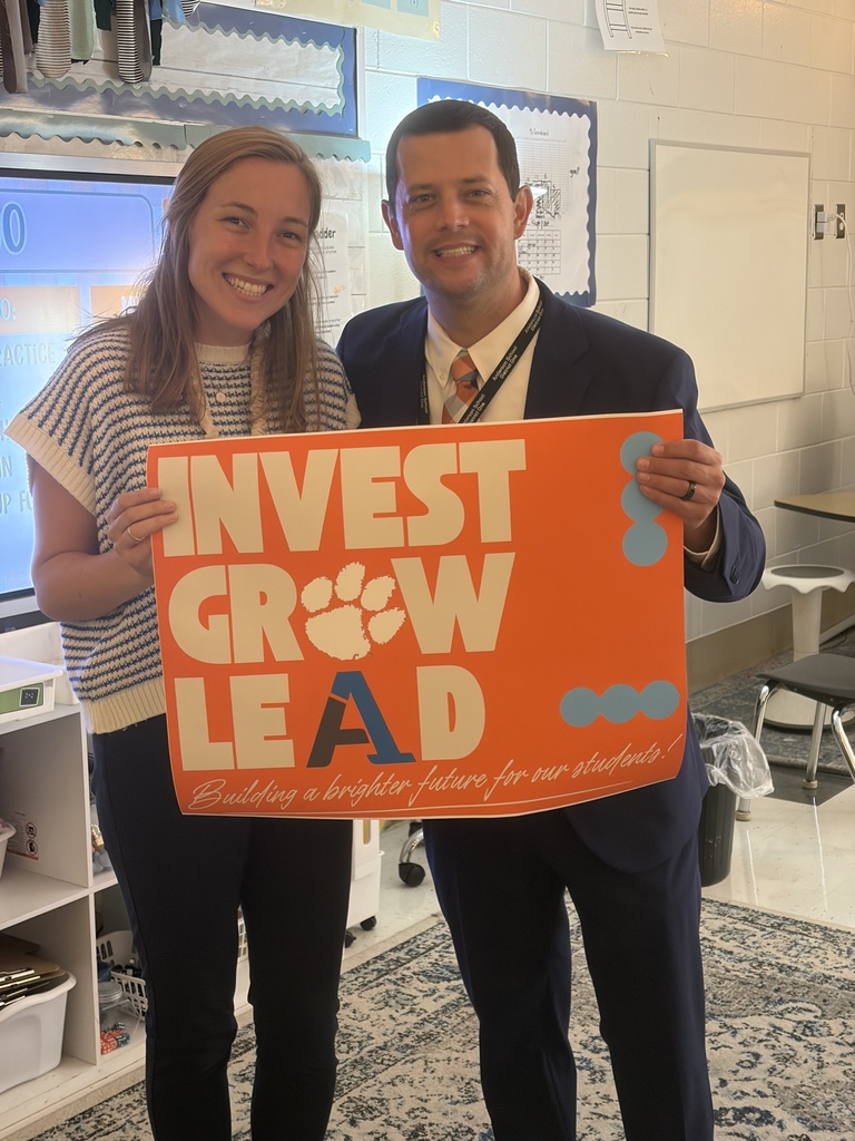A staff member poses for a picture with an educator with a sign that says Invest Grow Lead - Building a better future for our students