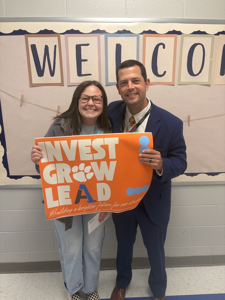 A staff member poses for a picture with an educator with a sign that says Invest Grow Lead - Building a better future for our students