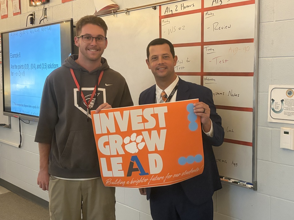 A staff member poses for a picture with an educator with a sign that says Invest Grow Lead - Building a better future for our students